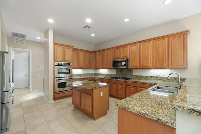 kitchen with light stone counters, sink, appliances with stainless steel finishes, and a center island