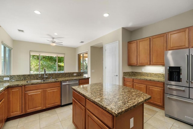 kitchen featuring ceiling fan, appliances with stainless steel finishes, stone countertops, a kitchen island, and sink