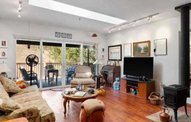 living room with track lighting, a wood stove, a skylight, and hardwood / wood-style flooring