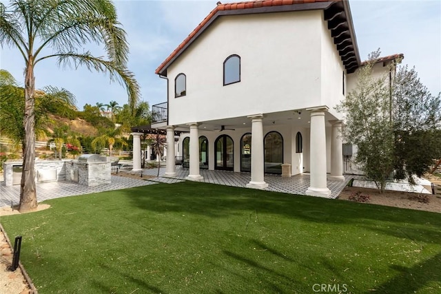 rear view of house with an outdoor kitchen, ceiling fan, a balcony, a yard, and a patio