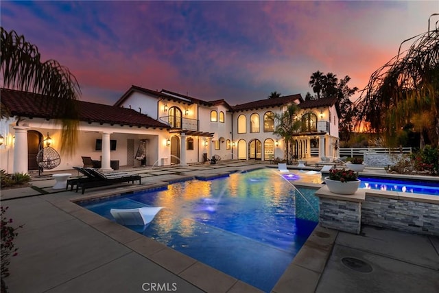 pool at dusk with a jacuzzi, a patio, and pool water feature