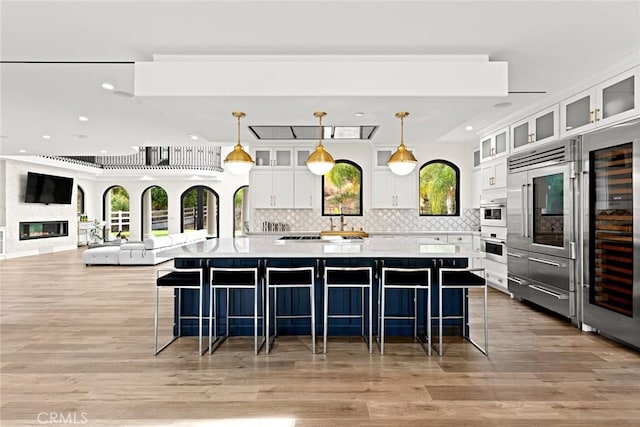 kitchen with tasteful backsplash, a large island with sink, pendant lighting, light hardwood / wood-style floors, and white cabinetry