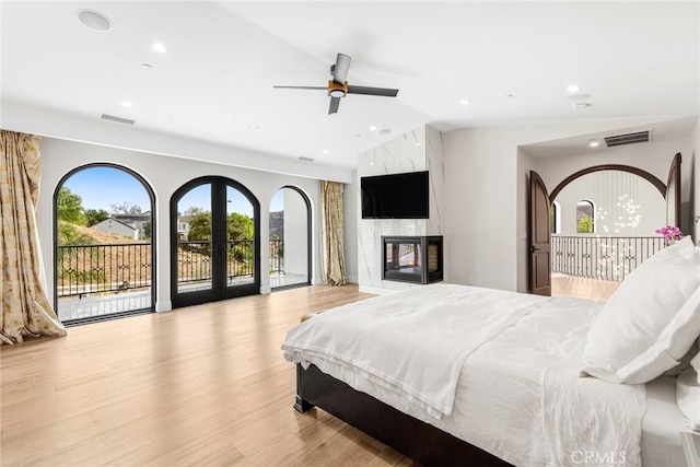 bedroom featuring access to outside, vaulted ceiling, ceiling fan, light wood-type flooring, and a fireplace