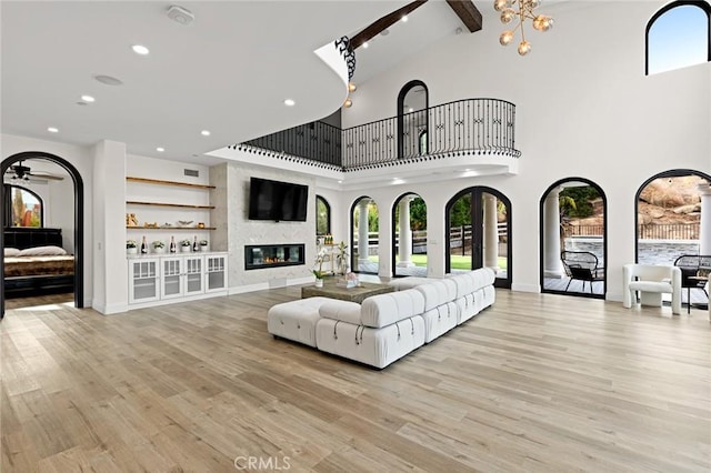 living room with ceiling fan with notable chandelier, a large fireplace, beam ceiling, high vaulted ceiling, and light hardwood / wood-style floors