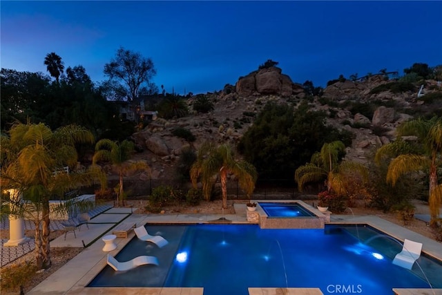 pool at dusk with pool water feature and an in ground hot tub