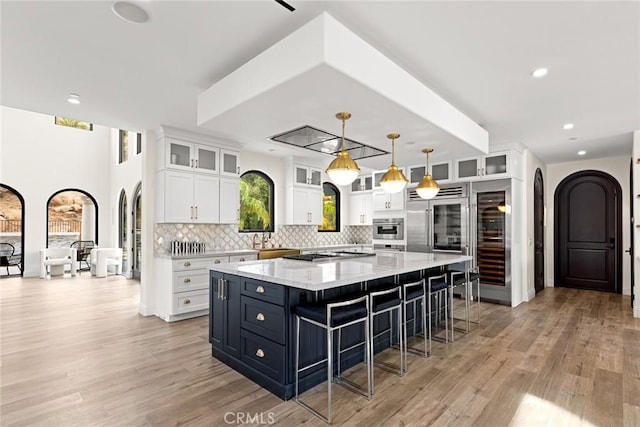 kitchen with pendant lighting, white cabinets, light stone countertops, a large island, and light hardwood / wood-style floors