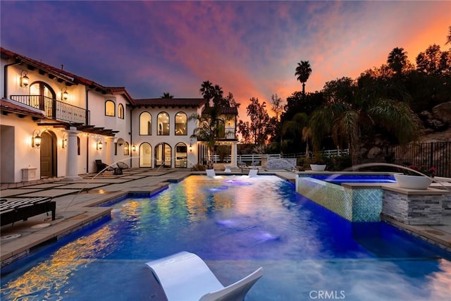 pool at dusk with an in ground hot tub, pool water feature, and a patio area