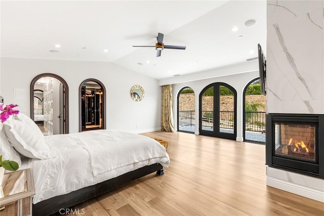 bedroom featuring a multi sided fireplace, vaulted ceiling, ceiling fan, access to exterior, and light hardwood / wood-style floors