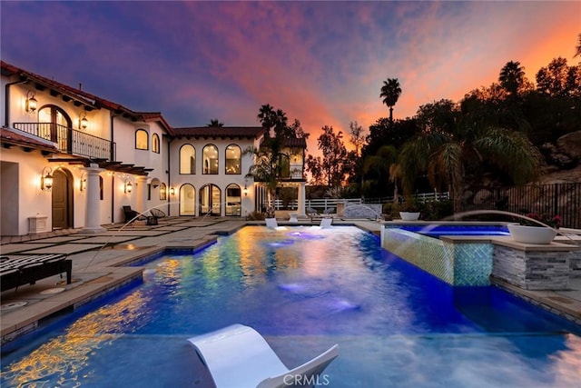 pool at dusk with pool water feature, a patio area, and an in ground hot tub