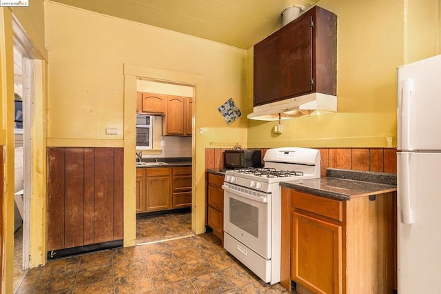 kitchen with sink, white appliances, backsplash, and wood walls