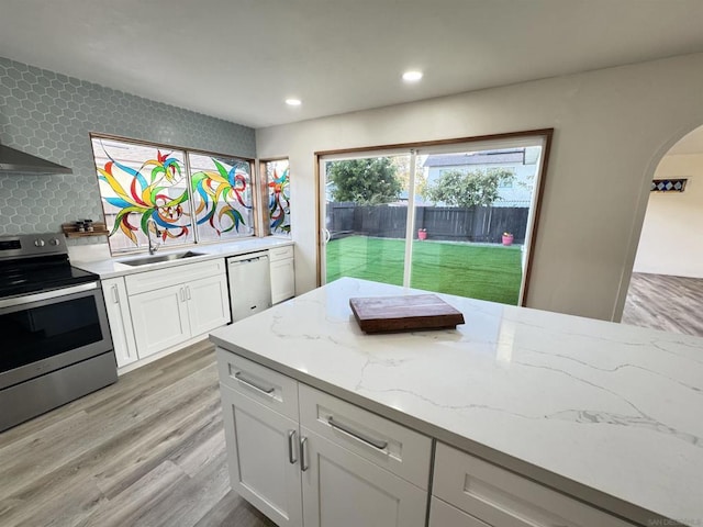 kitchen featuring appliances with stainless steel finishes, light stone counters, sink, light hardwood / wood-style flooring, and white cabinets