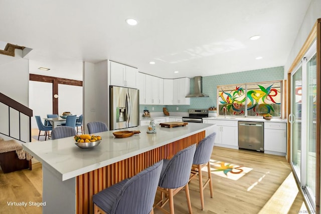 kitchen with wall chimney exhaust hood, stainless steel appliances, a center island, white cabinetry, and a breakfast bar area