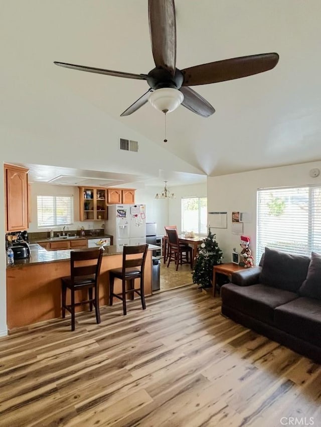 living area featuring ceiling fan with notable chandelier, high vaulted ceiling, visible vents, and light wood-style floors