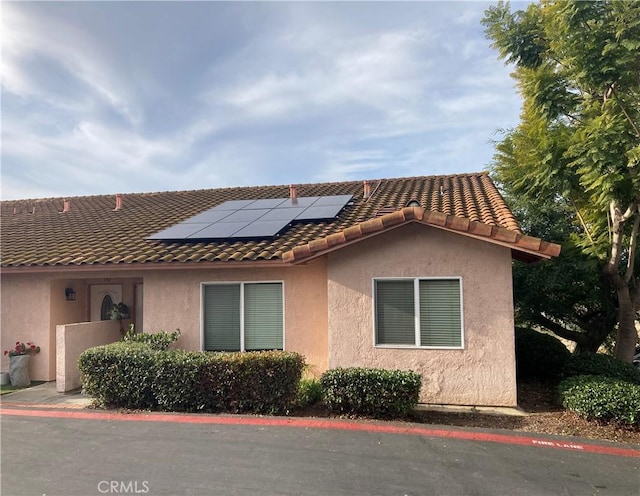 view of side of home with a tile roof, roof mounted solar panels, and stucco siding