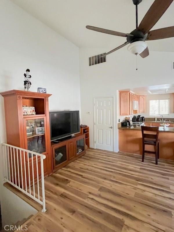 living area featuring a towering ceiling, light wood-style flooring, visible vents, and a ceiling fan