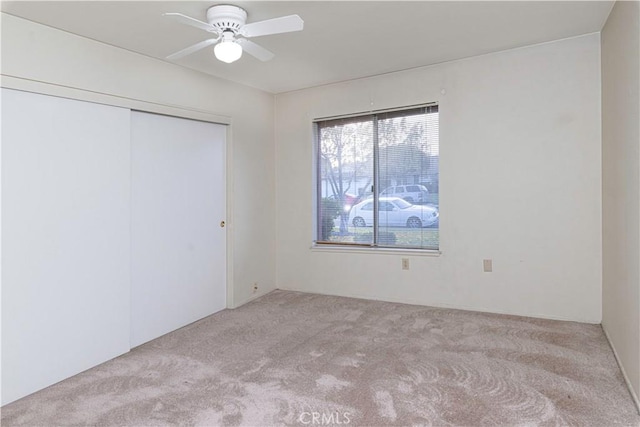 unfurnished bedroom with a closet, light colored carpet, and ceiling fan