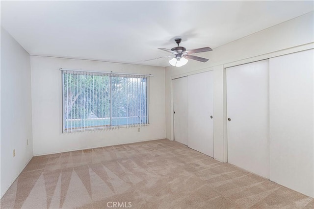 unfurnished bedroom with ceiling fan, light colored carpet, and two closets