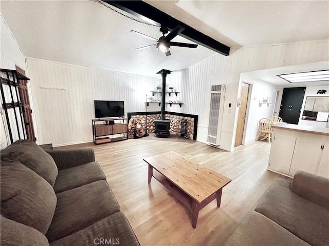 living room featuring a wood stove, ceiling fan, lofted ceiling with beams, wooden walls, and light wood-type flooring