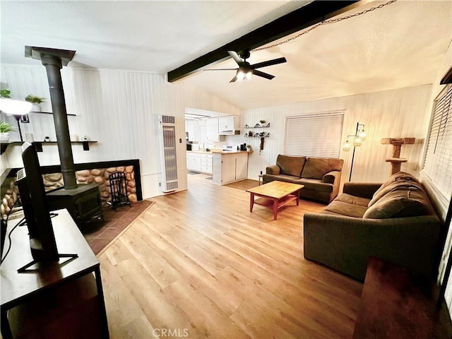 living room with a wood stove, light wood-style floors, ceiling fan, and vaulted ceiling with beams