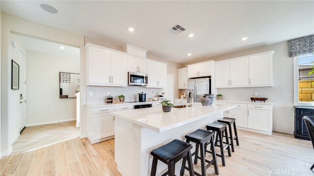 kitchen with a kitchen bar, white cabinetry, stainless steel appliances, and a kitchen island with sink