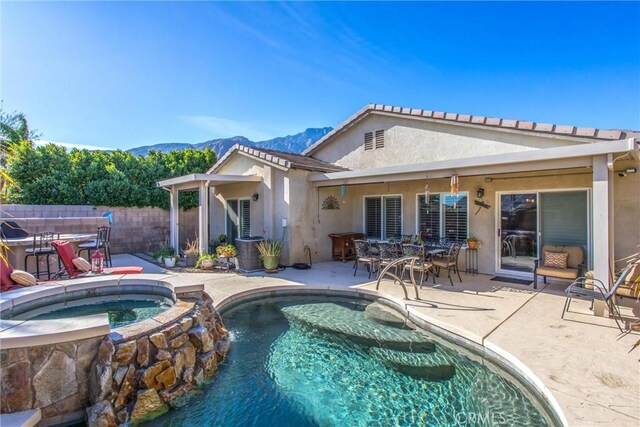 back of property with a swimming pool with hot tub, a patio area, and a mountain view