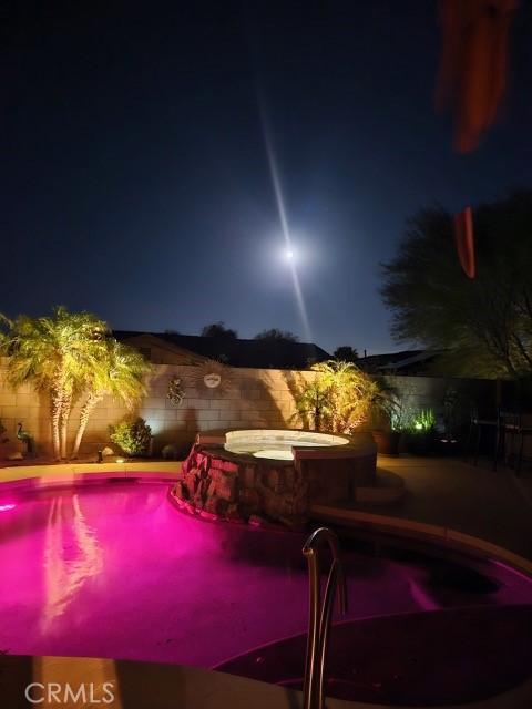 pool at night with a fenced backyard and a pool with connected hot tub