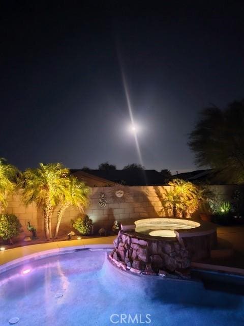 pool at twilight featuring a fenced in pool, a fenced backyard, and an in ground hot tub