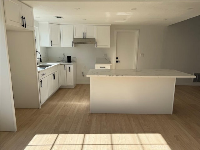 kitchen with white cabinets, a kitchen island, sink, and light hardwood / wood-style flooring