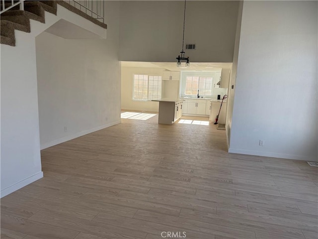 unfurnished living room with sink, a high ceiling, and light wood-type flooring