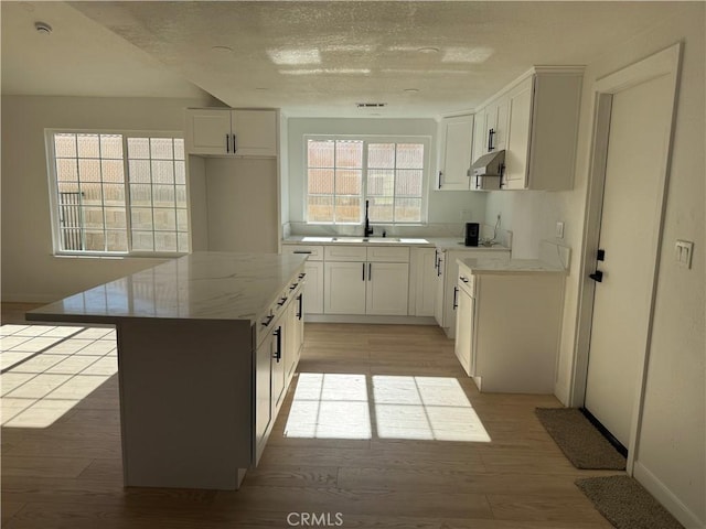 kitchen featuring a textured ceiling, sink, light hardwood / wood-style flooring, white cabinets, and a kitchen island