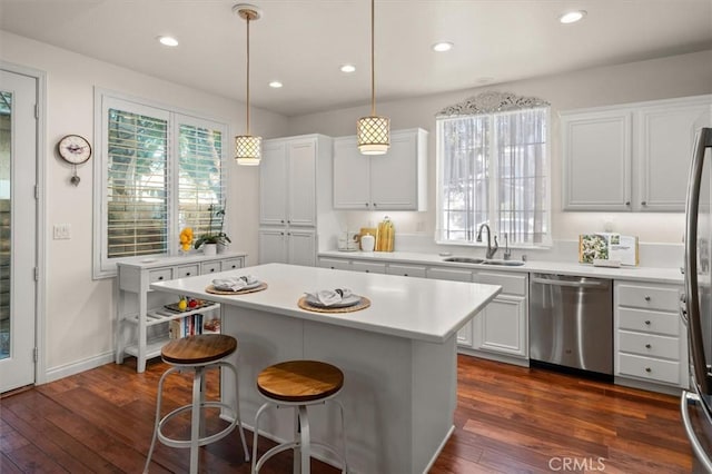 kitchen featuring a center island, white cabinetry, stainless steel appliances, sink, and hanging light fixtures