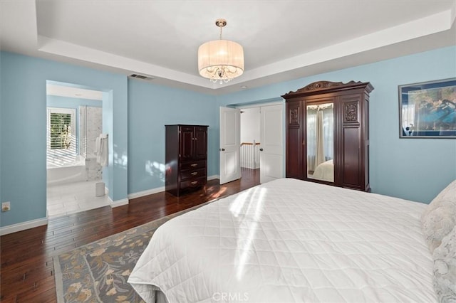 bedroom with ensuite bath, wood-type flooring, a raised ceiling, and a chandelier