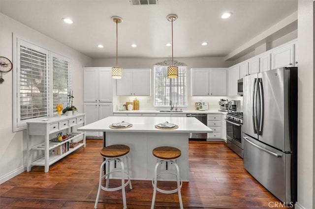 kitchen with decorative light fixtures, a center island, sink, stainless steel appliances, and white cabinets