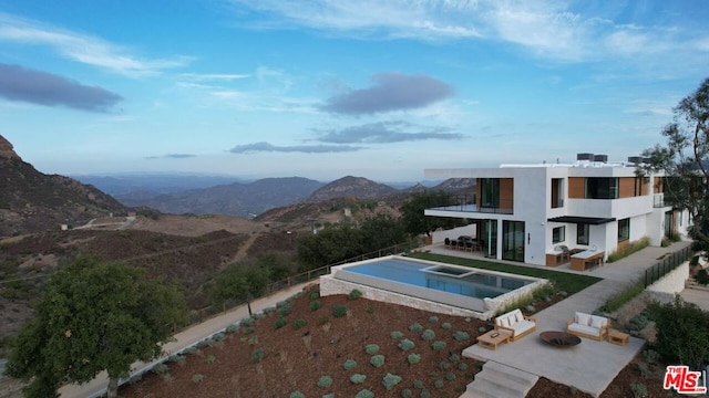 view of swimming pool with a patio area, an in ground hot tub, a mountain view, and an outdoor living space with a fire pit