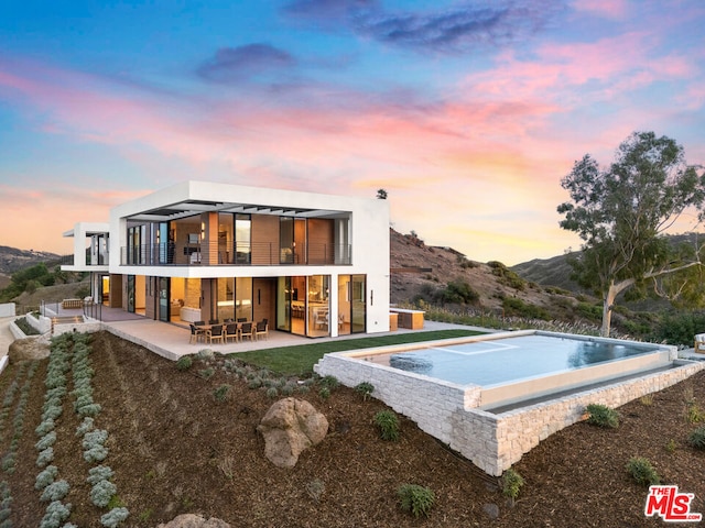 back house at dusk with a mountain view, a balcony, a patio, and area for grilling