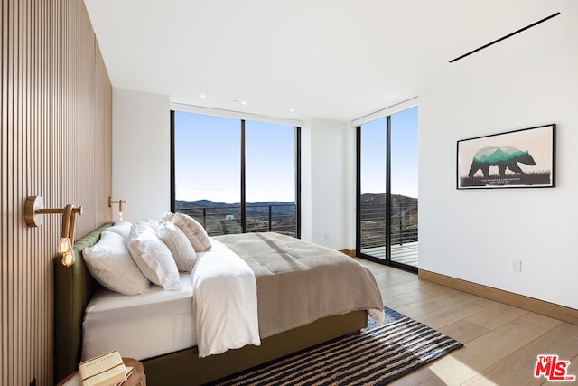 bedroom with light wood-type flooring, access to exterior, a wall of windows, and a mountain view