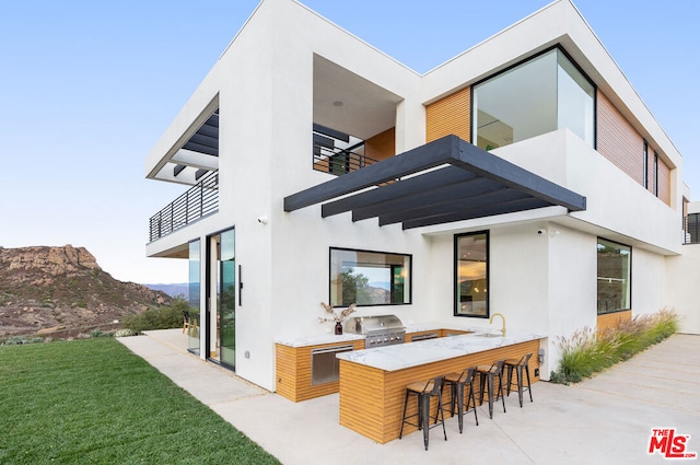 back of house featuring area for grilling, a lawn, an outdoor wet bar, a balcony, and a mountain view