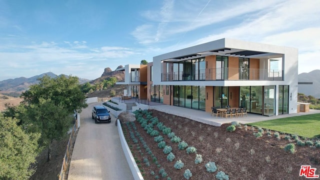 back of property featuring a mountain view, a balcony, and a patio