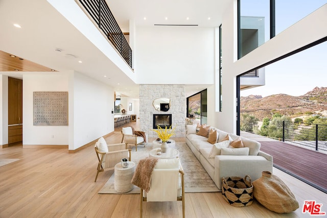 living room with light wood-type flooring, a fireplace, a mountain view, and a towering ceiling