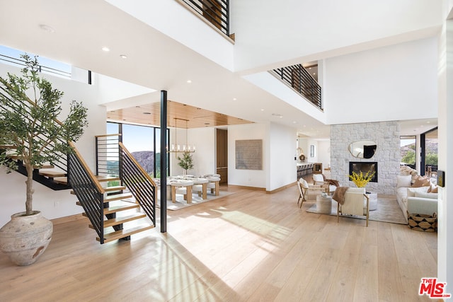 living room with light wood-type flooring, a fireplace, a wealth of natural light, and a high ceiling