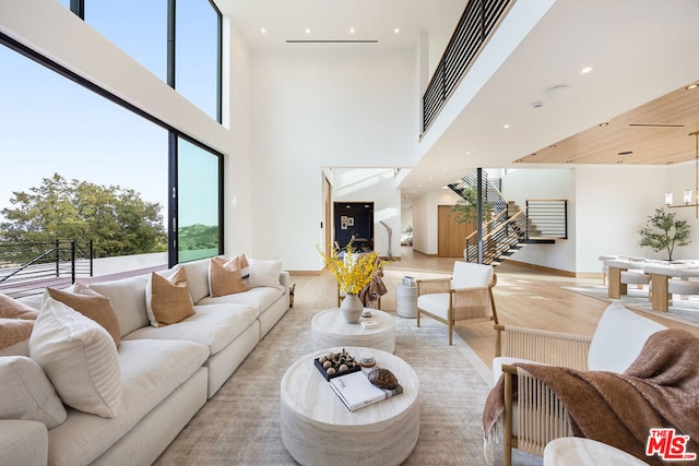 living room with light hardwood / wood-style floors, a high ceiling, a chandelier, and a healthy amount of sunlight