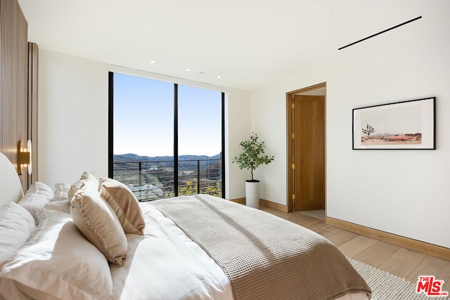 bedroom featuring a mountain view, multiple windows, expansive windows, and light wood-type flooring