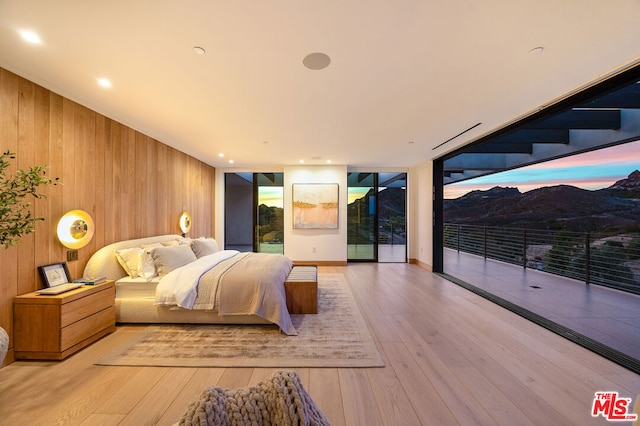 bedroom featuring access to exterior, floor to ceiling windows, light hardwood / wood-style flooring, and wooden walls