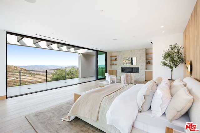 bedroom featuring a wall of windows, a stone fireplace, access to exterior, a mountain view, and light hardwood / wood-style flooring