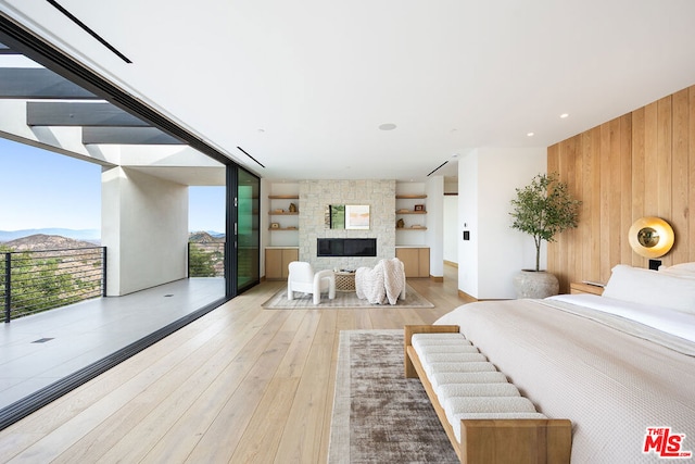 bedroom with a fireplace, floor to ceiling windows, wooden walls, a mountain view, and light hardwood / wood-style flooring