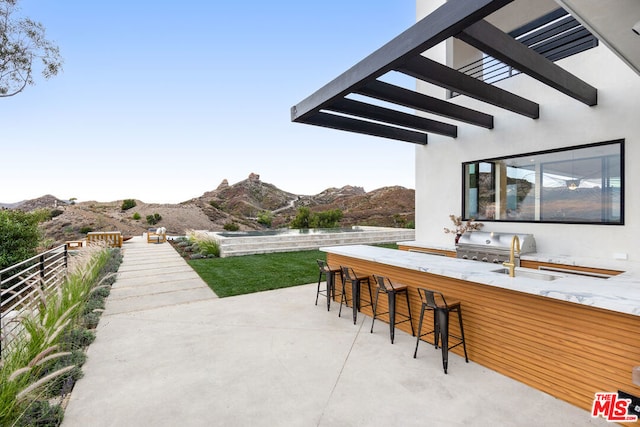 view of patio with grilling area, a mountain view, and a wet bar