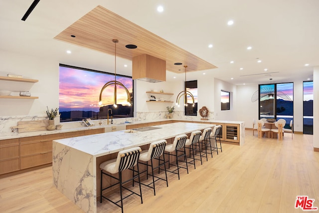 kitchen featuring light stone countertops, hanging light fixtures, kitchen peninsula, light wood-type flooring, and a breakfast bar area