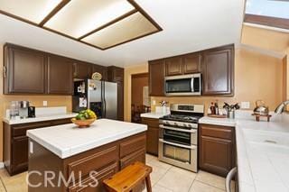 kitchen featuring dark brown cabinetry, light tile patterned floors, stainless steel appliances, and a kitchen island