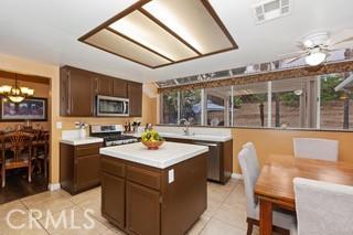 kitchen with ceiling fan with notable chandelier, light tile patterned flooring, a kitchen island, and appliances with stainless steel finishes