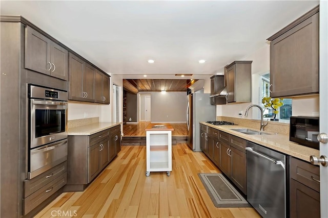 kitchen with appliances with stainless steel finishes, light hardwood / wood-style flooring, dark brown cabinets, and sink